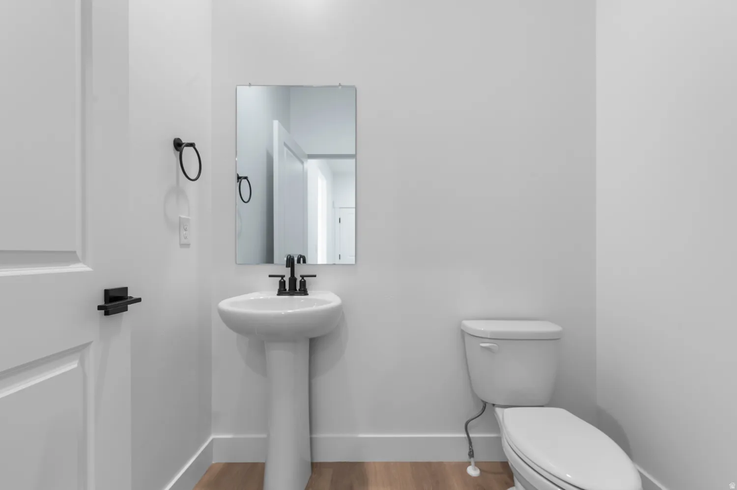 Pedestal sink with matte black faucet, wall-mounted mirror, and wood-finish flooring