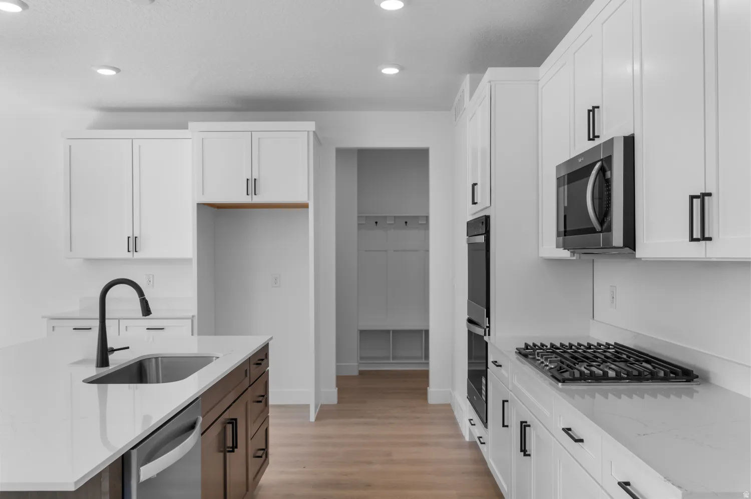 Modern kitchen featuring white shaker cabinetry, quartz countertops, a gas range, built-in microwave, and a large island with an undermount sink and matte black faucet