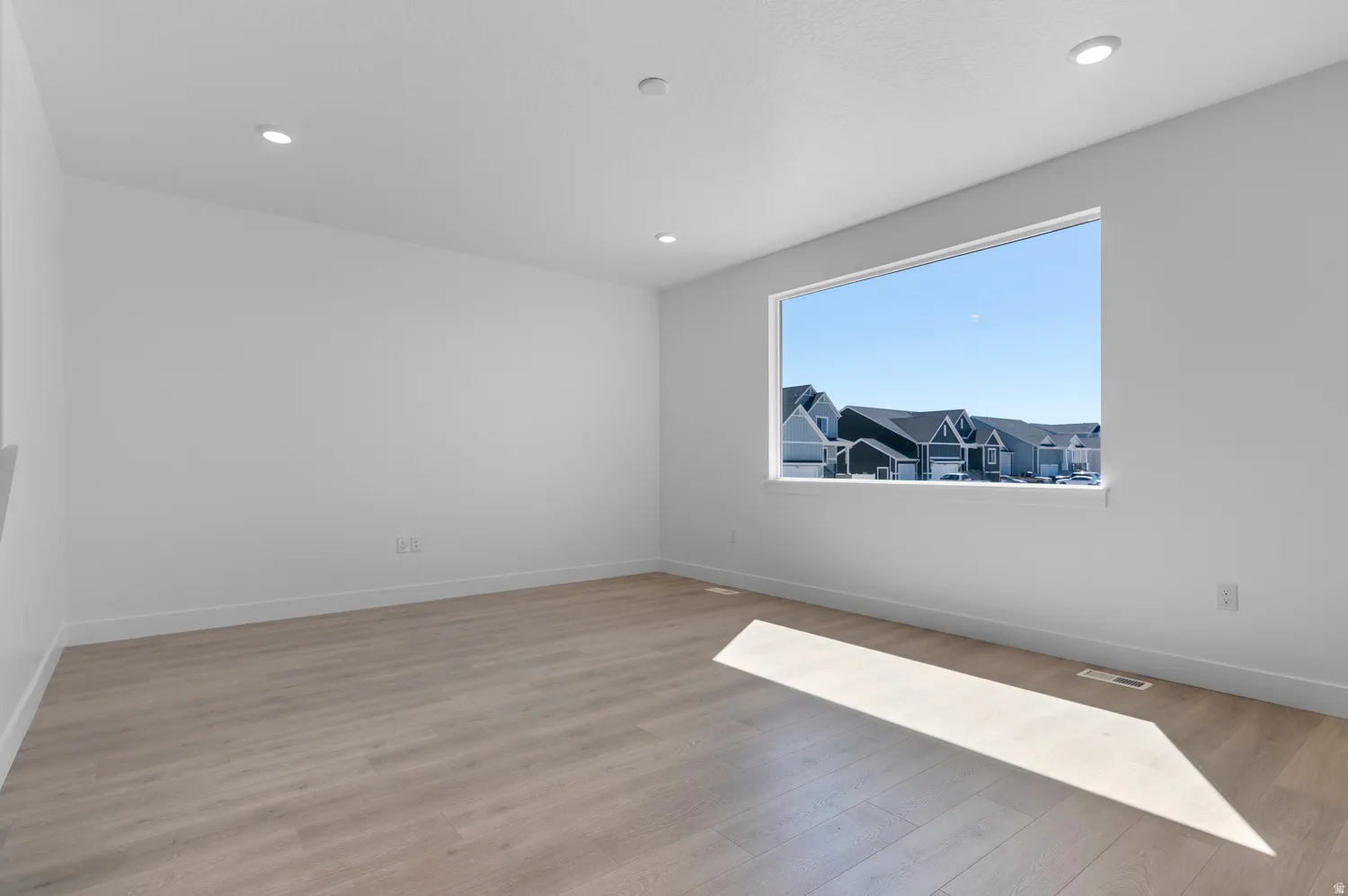 Spacious room featuring a large horizontal window, recessed lighting, light wood-finish flooring, white baseboards, and neutral wall finishes