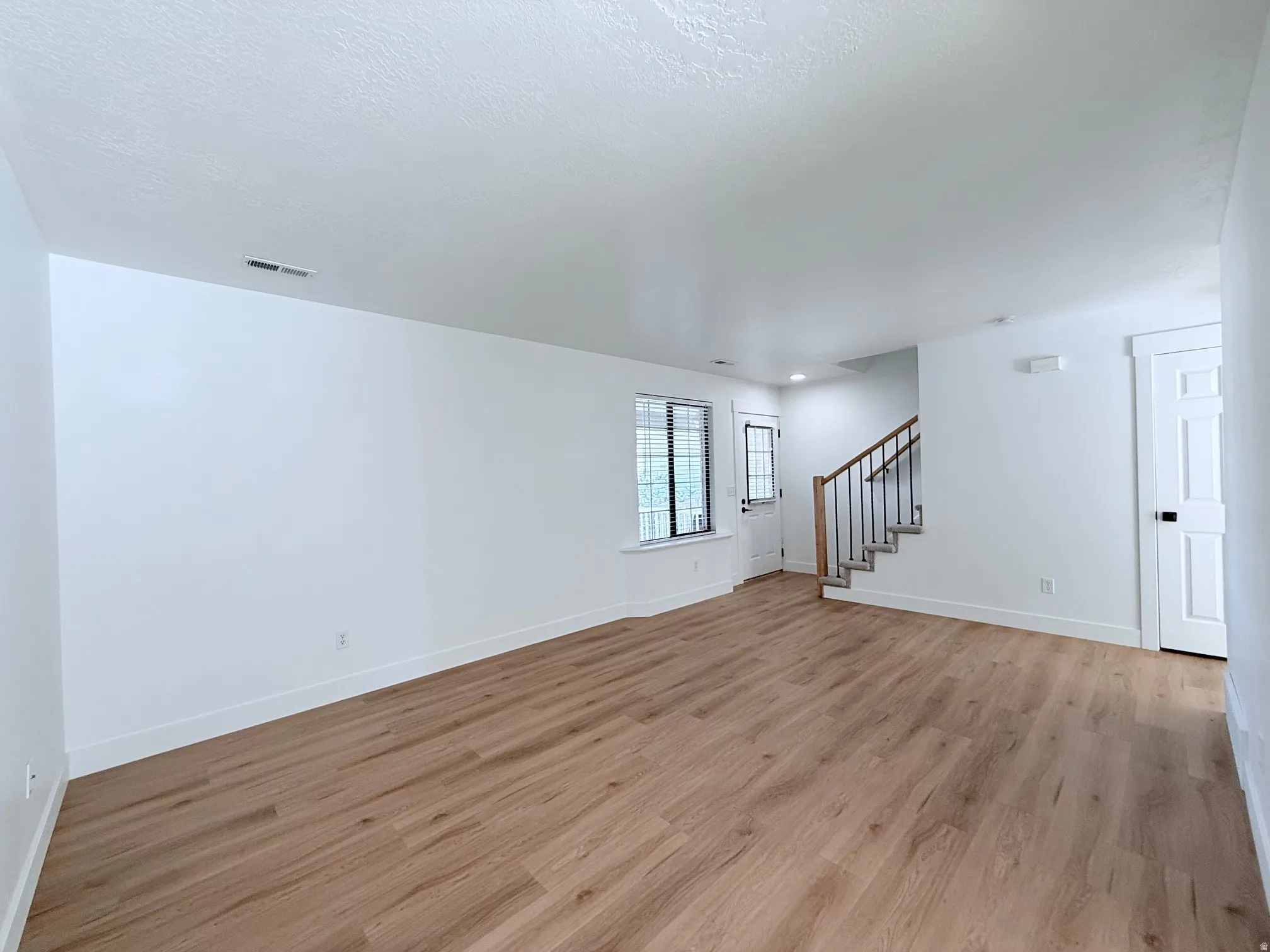 Spacious room featuring wood-finish flooring, white walls, and a staircase with wood and metal railings