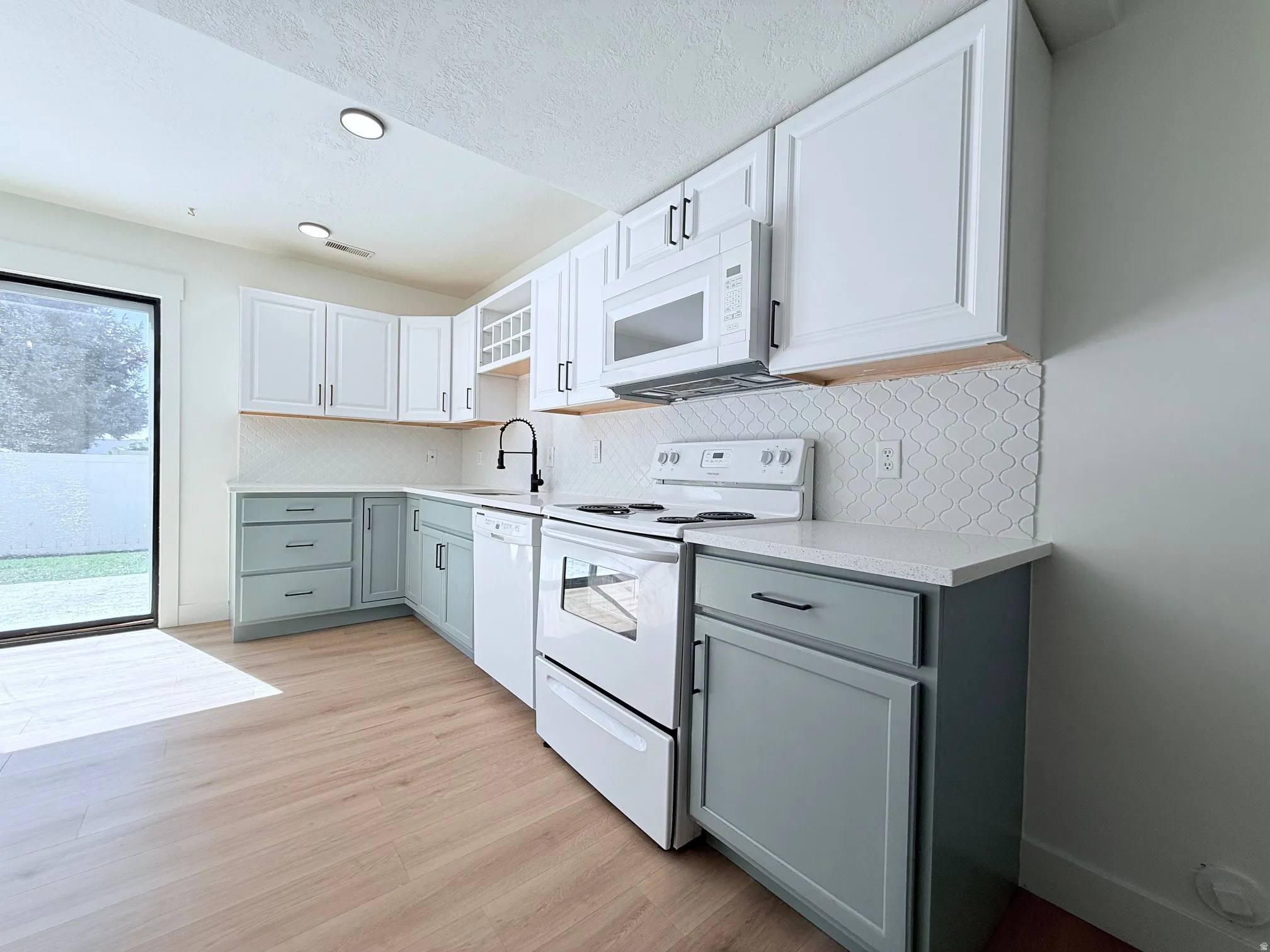 White upper cabinetry, light wood-finish flooring, white subway tile backsplash, white quartz countertops, and a built-in microwave