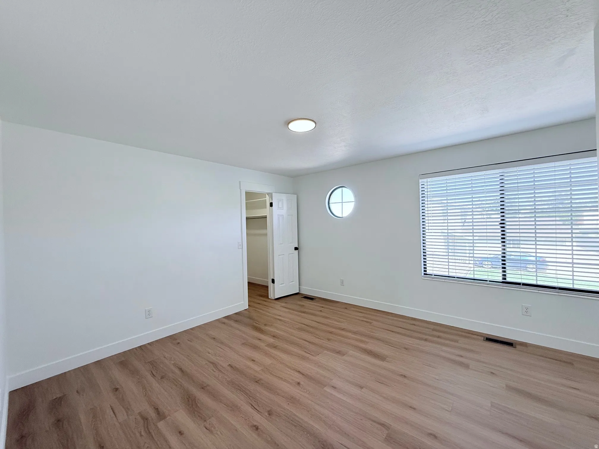 Wood-finish flooring, white walls, and a large window with blinds