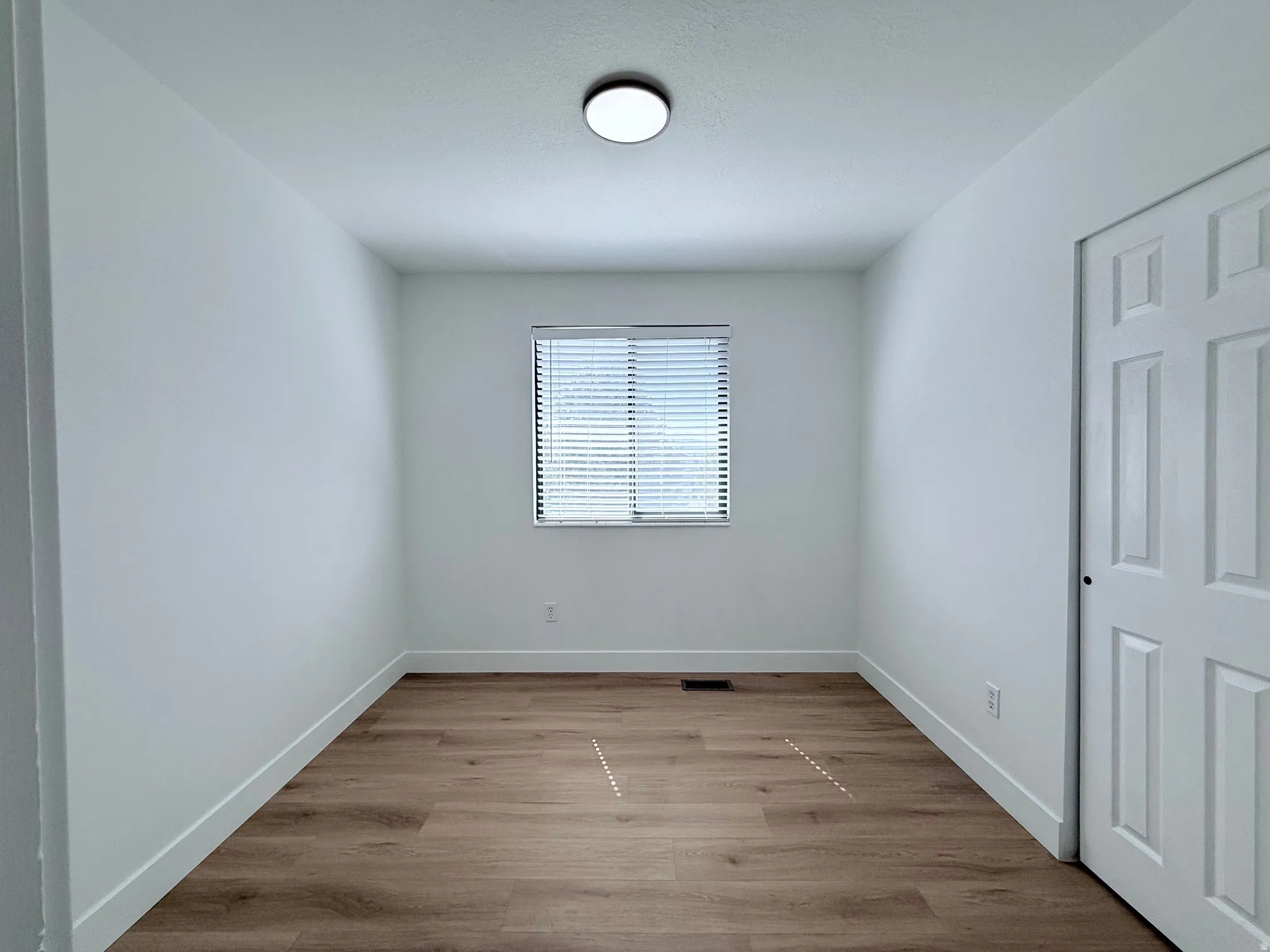 Recessed window with blinds, wood-finish flooring, white walls, and a flush-mount ceiling light