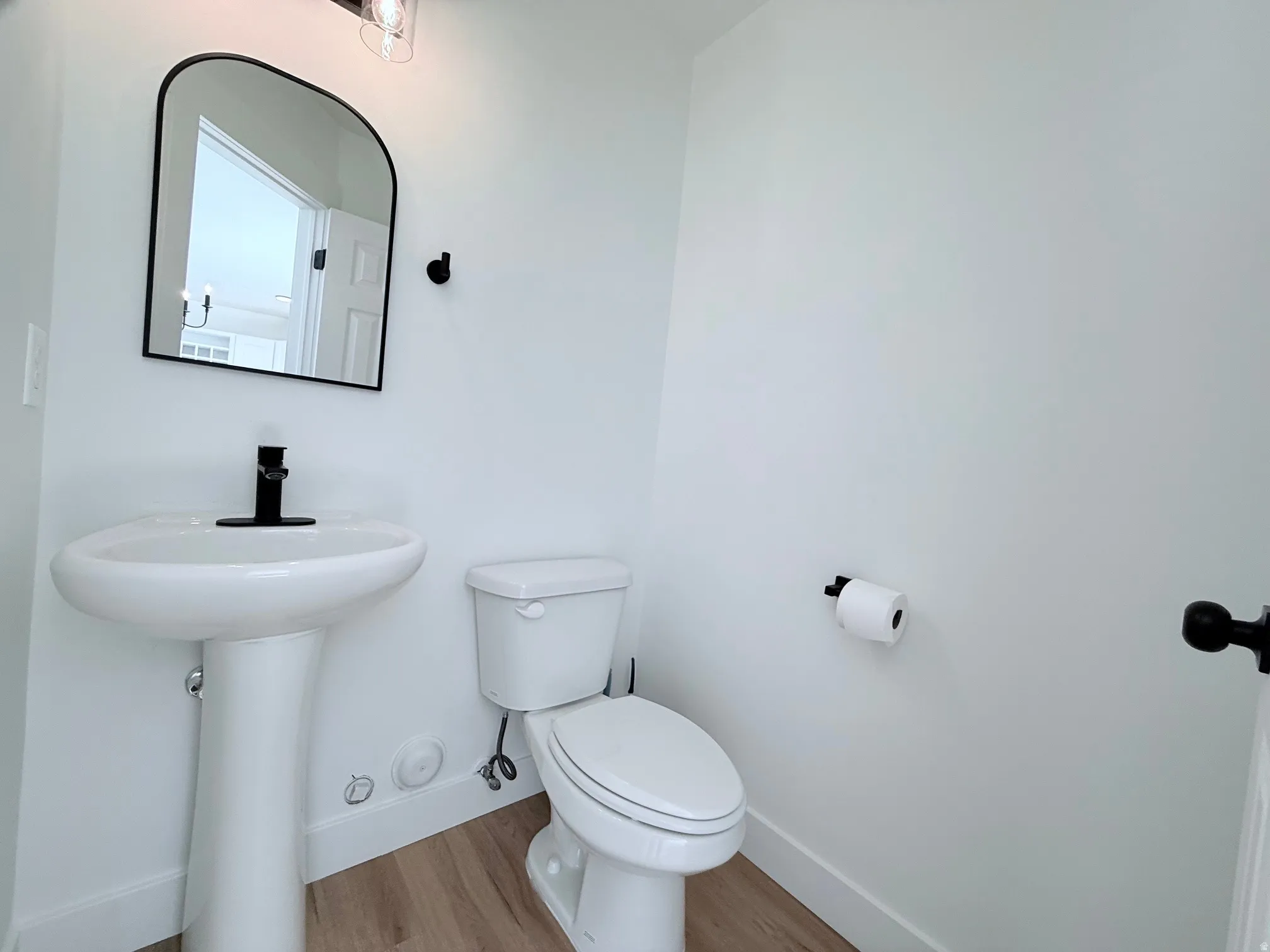 Pedestal sink with a matte black faucet, complementary arched mirror, and wood-finish flooring