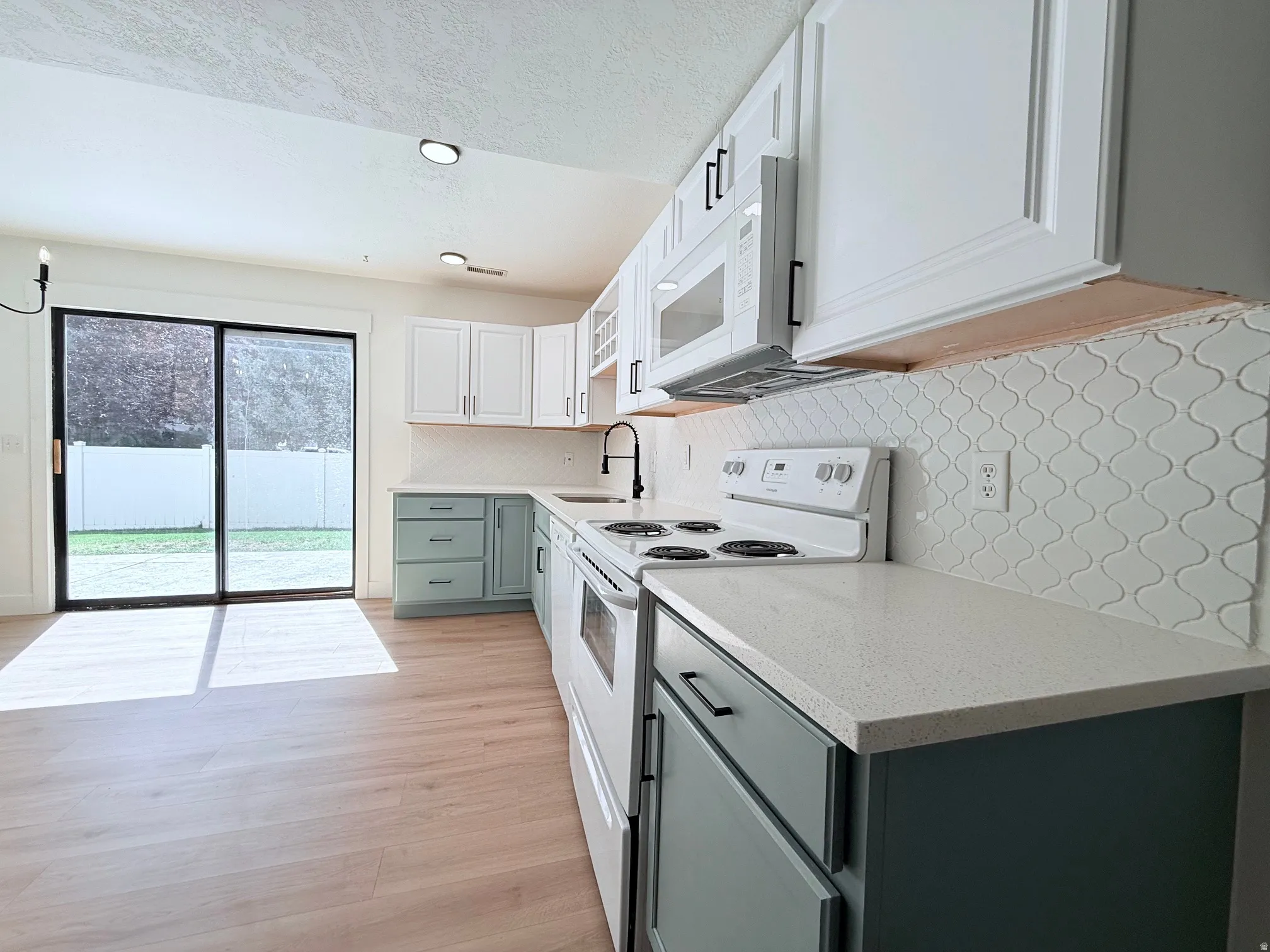 Kitchen featuring wood-finish flooring, two-tone cabinetry, light countertops, arabesque tile backsplash, and a sliding glass door to the exterior