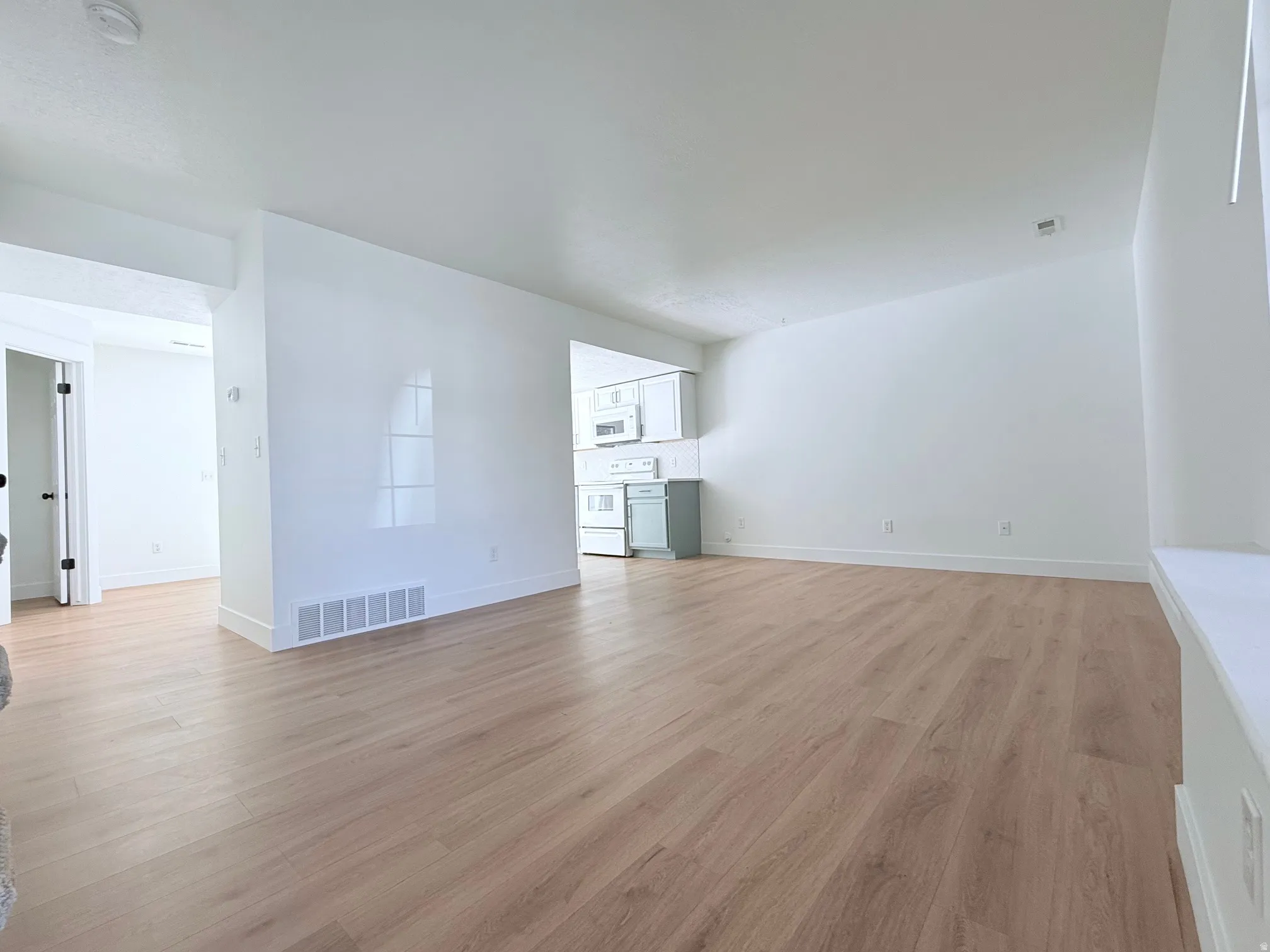 Bright, open living space featuring wood-finish flooring throughout, clean white walls, and abundant natural light from multiple windows