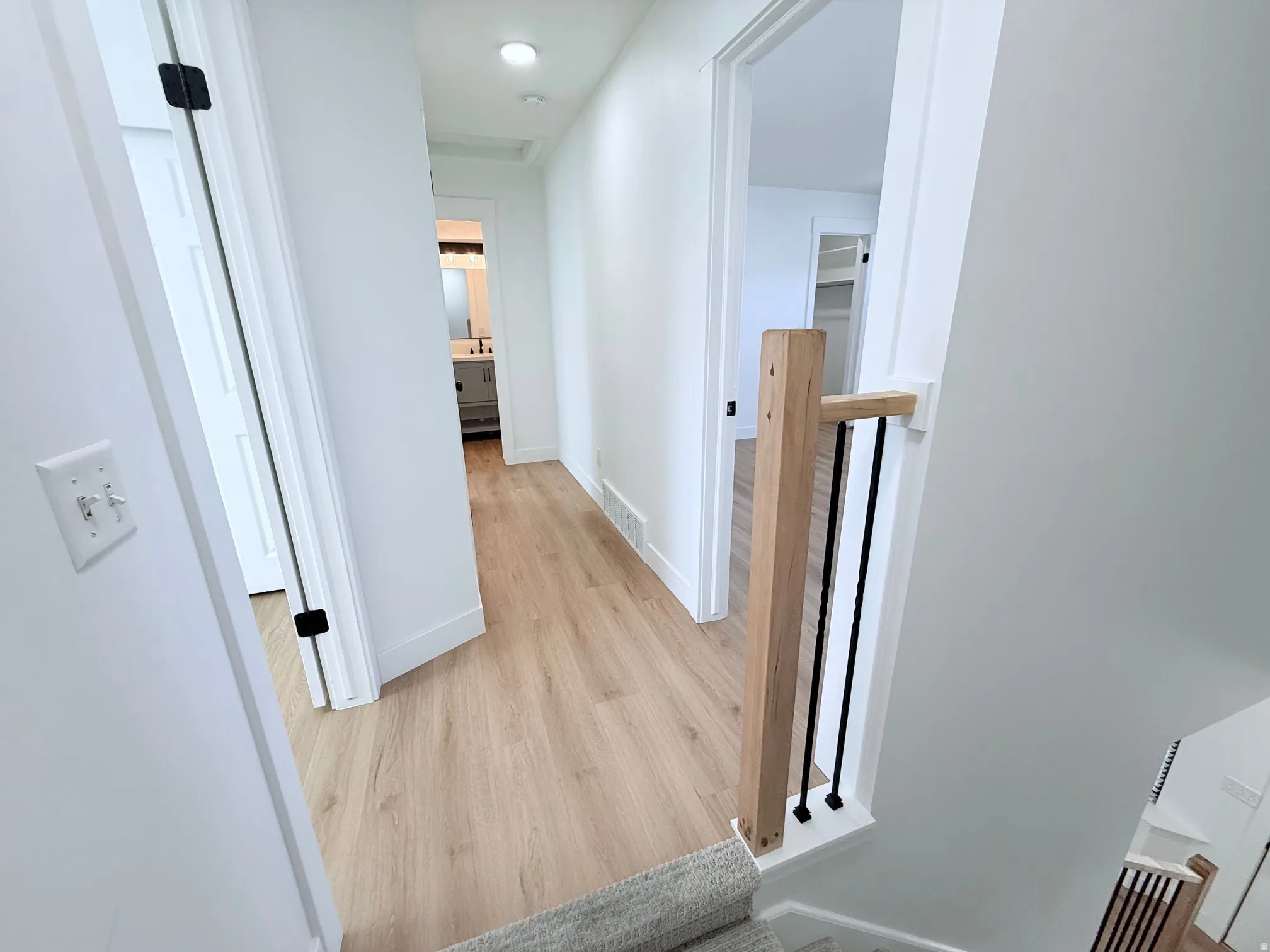Light wood-finish flooring, white walls, recessed ceiling lighting, and a contemporary wood newel post with black metal balusters