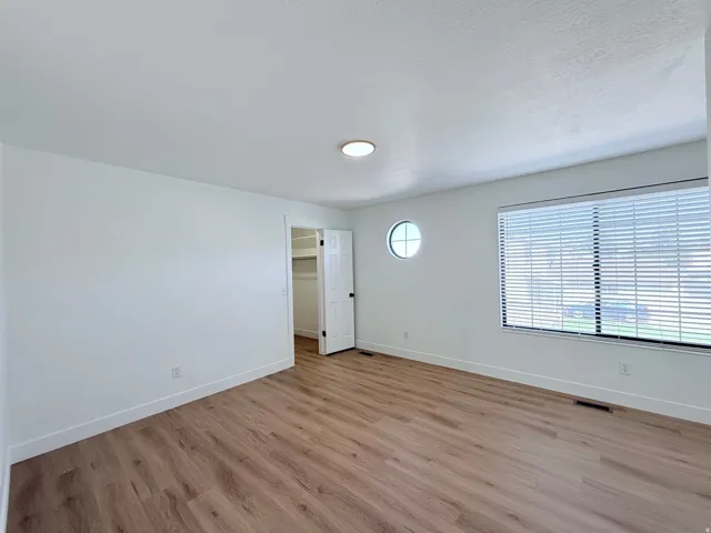 Wood-finish flooring, white walls, and a large window with blinds