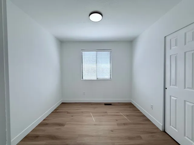 Recessed window with blinds, wood-finish flooring, white walls, and a flush-mount ceiling light