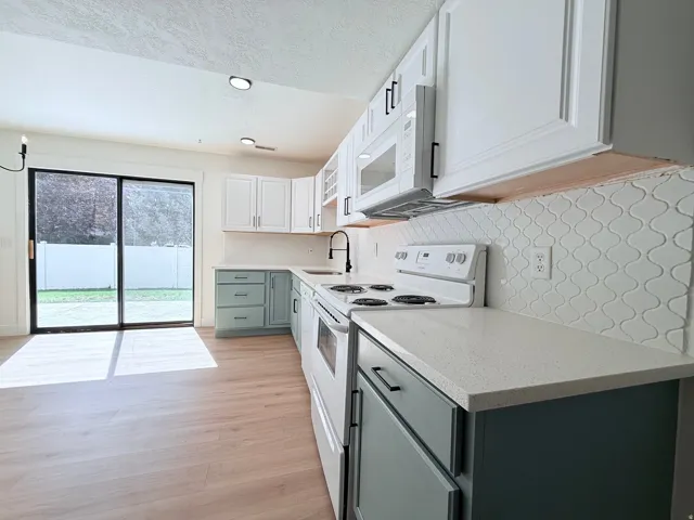 Kitchen featuring wood-finish flooring, two-tone cabinetry, light countertops, arabesque tile backsplash, and a sliding glass door to the exterior