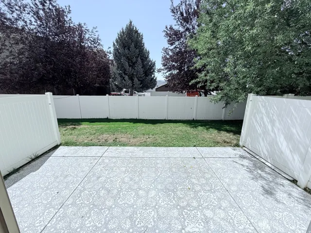 Fenced backyard featuring a concrete patio with control joints, manicured lawn, and mature trees providing natural screening and shade