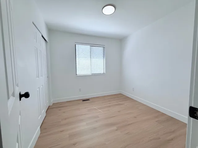 Light wood-finish flooring, white walls, and a window with blinds provide a bright interior