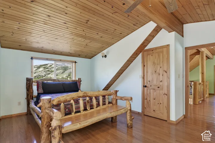 Room featuring wood-finish flooring, a sloped wood-paneled ceiling, a window with mountain scenery, a wood-paneled door, and exposed wood beams