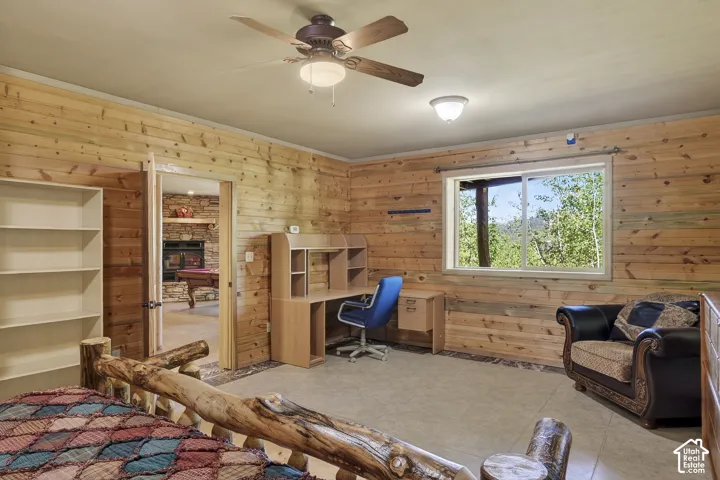 Room featuring extensive wood paneling, a large window with natural light, a ceiling fan with integrated lighting, and tile flooring