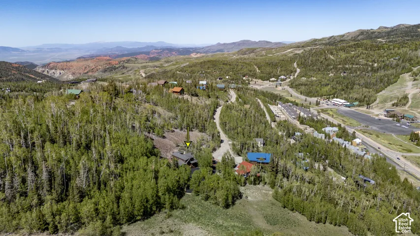 Mountain property surrounded by dense forest, featuring a prominent red roof and a rustic exterior