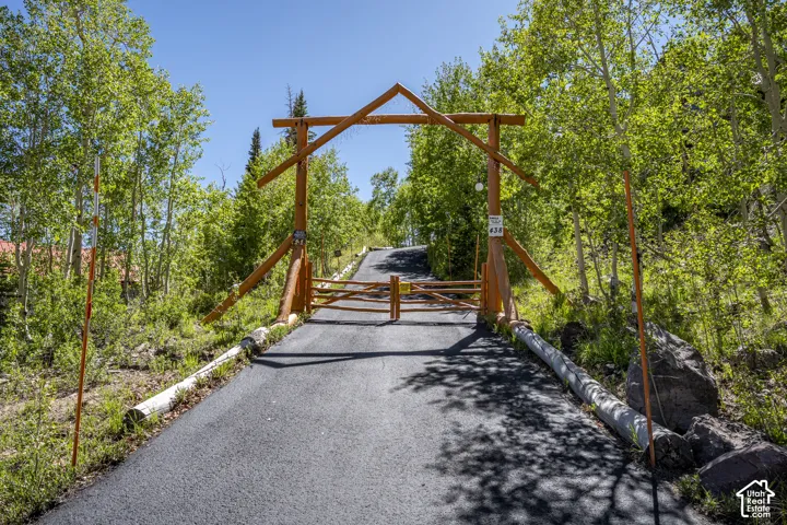 Paved driveway entrance with a rustic wooden gate and overhead archway, framed by mature trees