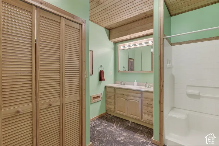 Bathroom featuring a double vanity with light wood cabinetry, a large wall-mounted mirror, and a coordinated wood-finish ceiling