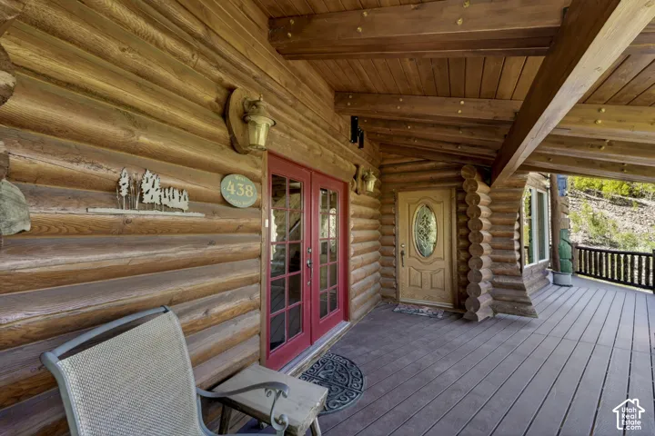 Log cabin exterior featuring a covered porch with wood-finish decking, exposed wood beams, and a decorative wood wall sconce