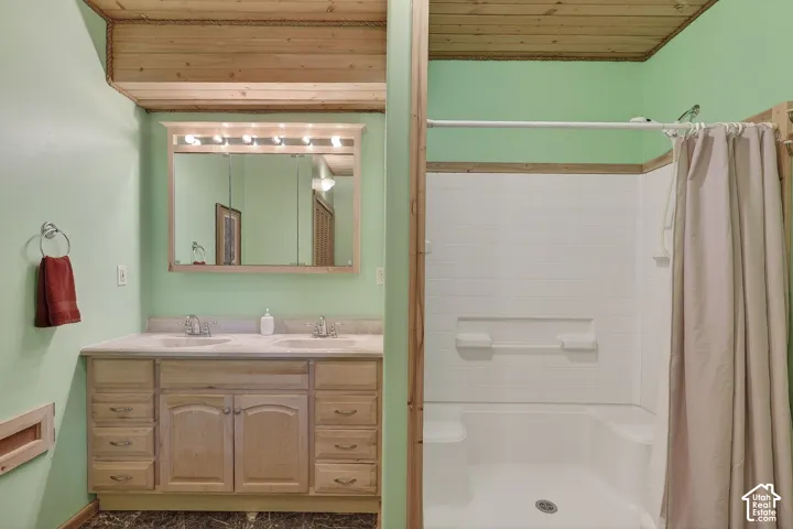 Bathroom featuring a dual-sink vanity with light wood cabinetry and a framed mirror with integrated lighting
