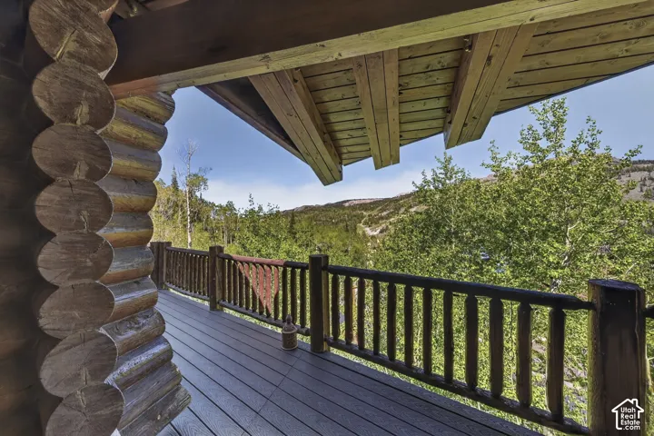 Rustic log construction balcony featuring a composite deck surface, log railing, and exposed wood ceiling beams