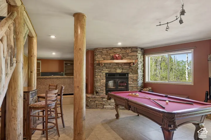 Spacious recreation room featuring a stone fireplace with hearth, a built-in bar, and log structural columns