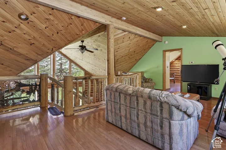 Open-concept living space featuring wood-finish flooring, natural wood paneled ceilings, and log railing accents