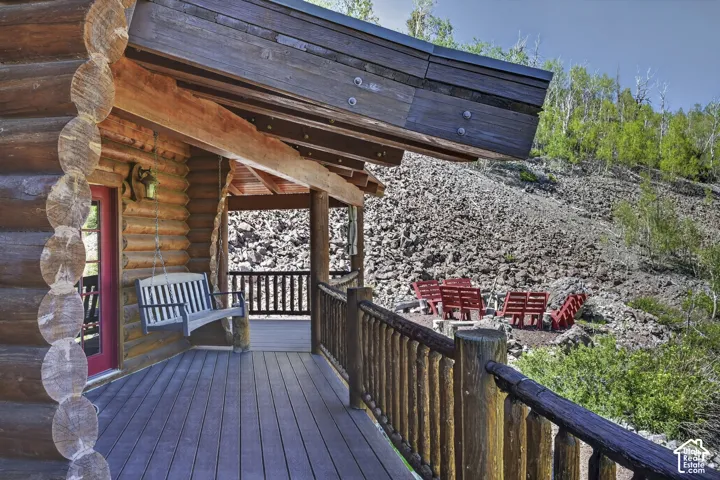 Expansive log cabin porch featuring a durable composite deck, rustic log railings, and a red entry door