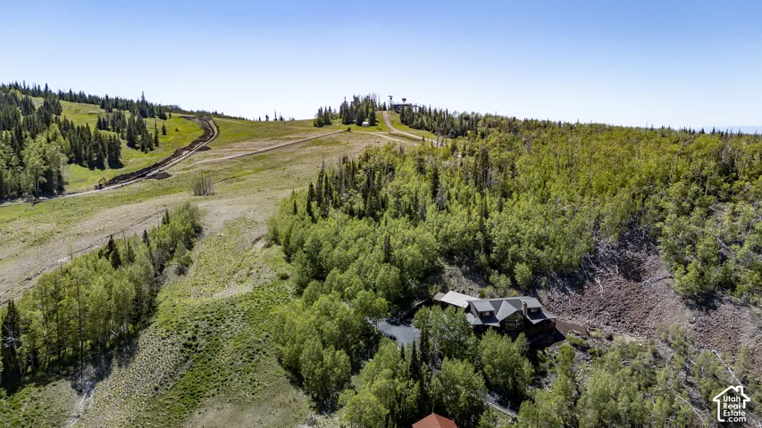 Hillside property surrounded by mature trees, featuring a multi-level structure and a gravel drive