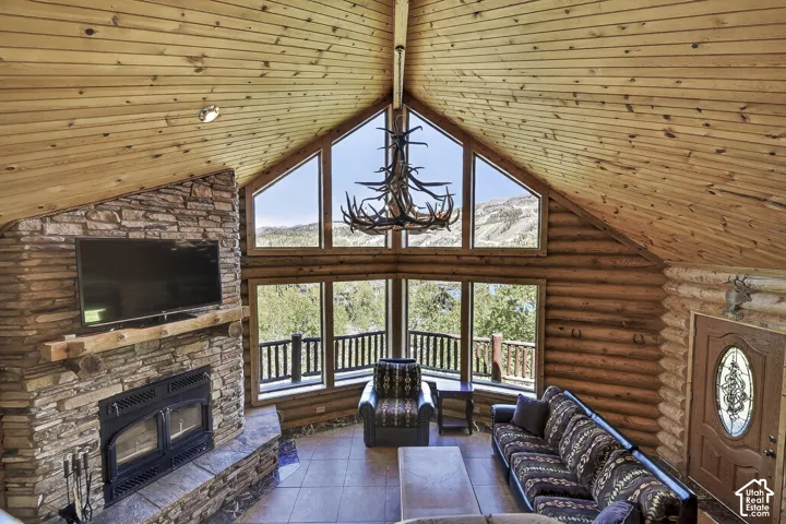 Vaulted ceiling with wood-finish planks, stone-clad fireplace with wood mantle, and a large window array with mountain scenery