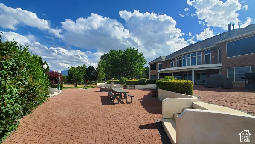 Extensive brick paver patio featuring a terraced design, a landscaped perimeter, and a multi-level architectural backdrop with abundant windows