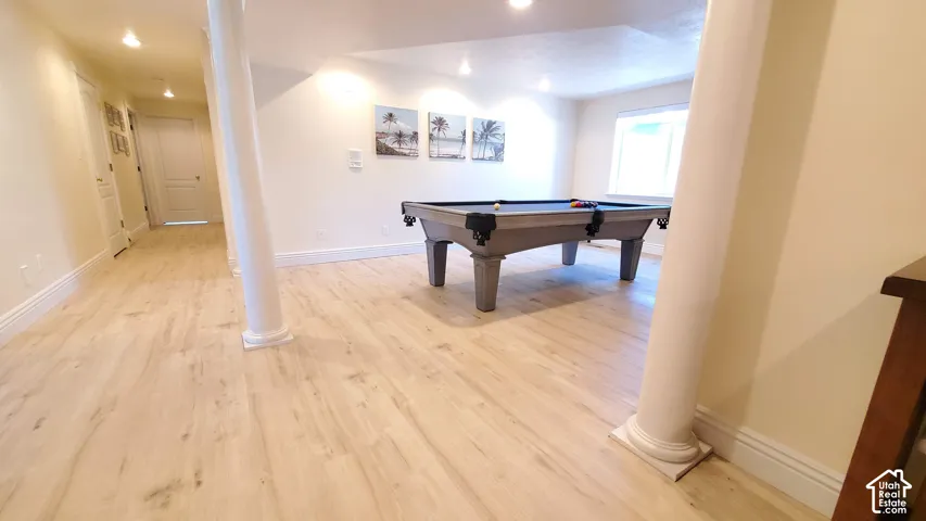 Spacious recreation area featuring light wood-finish flooring, recessed lighting, and a window providing natural light