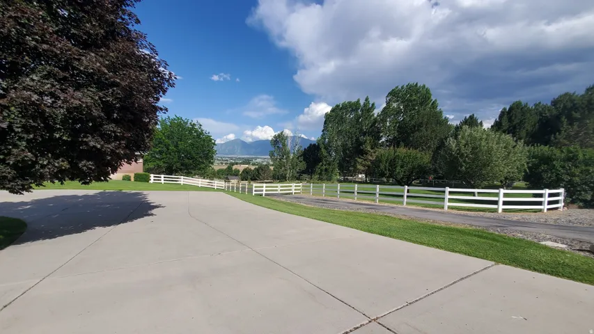 Paved driveway bordered by a manicured lawn and white fencing