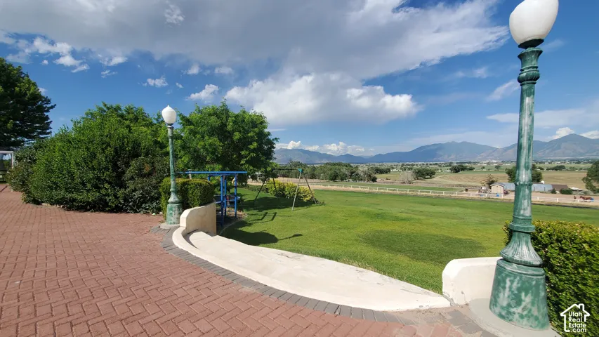 Expansive green lawn framed by mature landscaping, brick paver patio, decorative street lamps, and distant mountain ranges