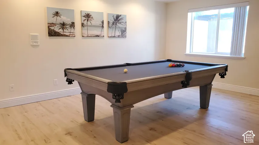 Recreation room featuring light wood-finish flooring, ample wall space, and a large window with vertical blinds