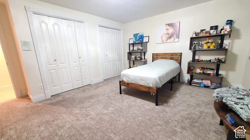 Carpeted room featuring two sets of bi-fold closet doors with decorative trim, a textured headboard, and built-in shelving units