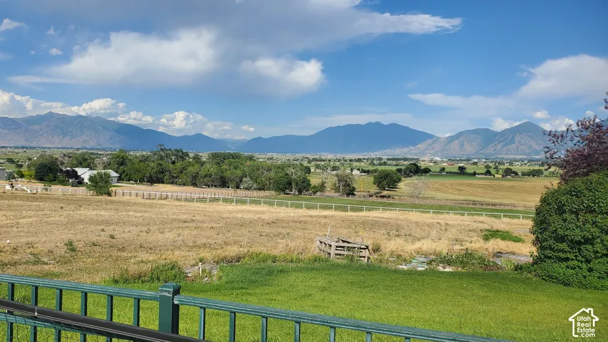 Expansive landscape featuring distant mountains, agricultural fields, scattered trees, a green lawn, and a dark green railing