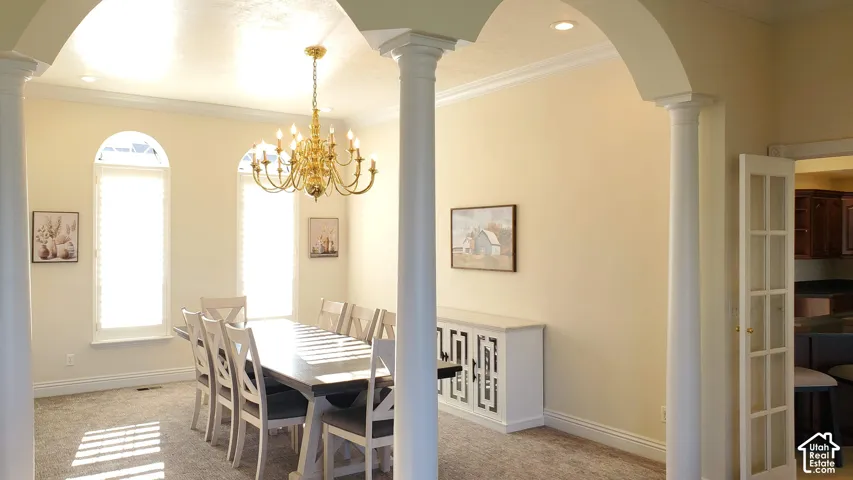 Dining area featuring arched windows with internal shutters, a gold-toned chandelier, recessed lighting, and crown molding