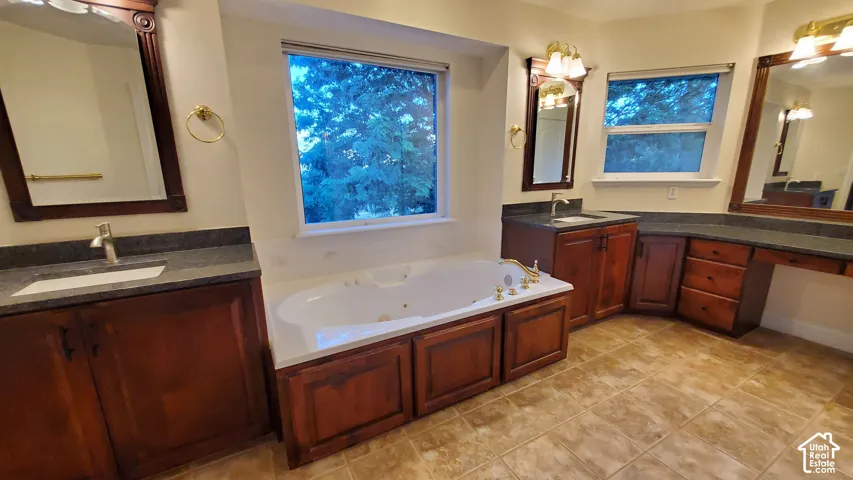 Spacious Master bathroom featuring a built-in jetted tub, two wood-finish vanities with undermount sinks, Granite countertops, and large framed mirrors