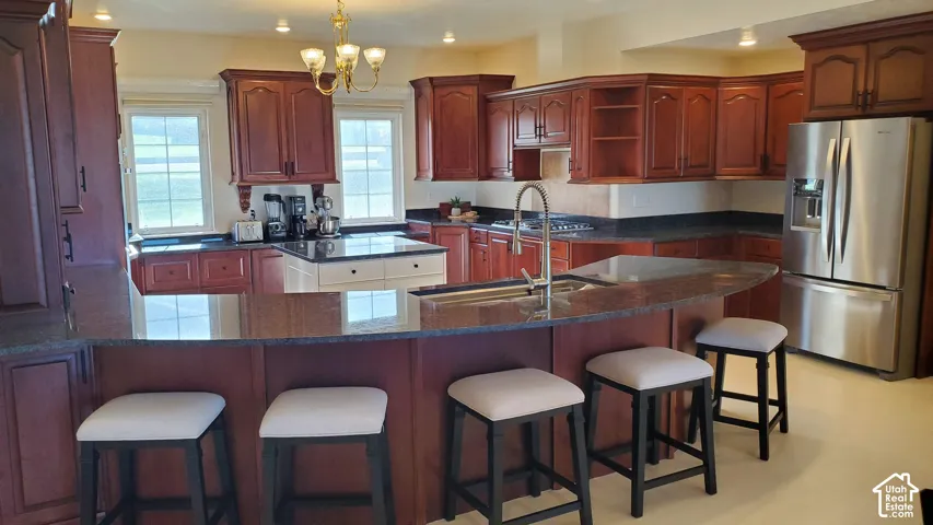 Kitchen featuring rich wood cabinetry, Granite countertops, a stainless steel French door refrigerator, a central island with a built-in sink, and integrated bar seating