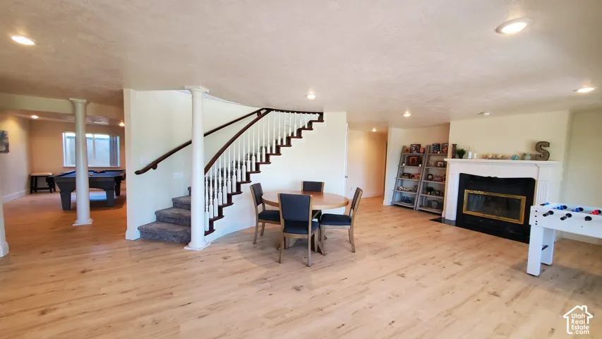 Spacious lower level featuring wood-finish flooring, a traditional fireplace with white mantel, recessed lighting, and a carpeted staircase with white balusters and dark wood handrails