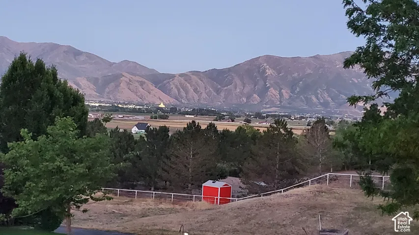 Expansive outdoor area featuring a white fence, mature trees, and a distant mountain range