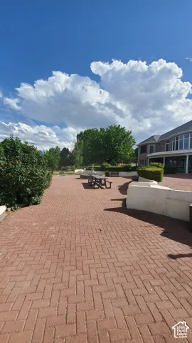 Expansive brick paver patio featuring a herringbone pattern, bordered by raised planters with mature shrubbery and trees