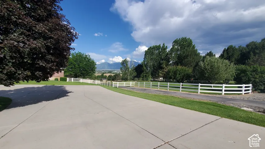 Paved driveway bordered by a manicured lawn and white fencing