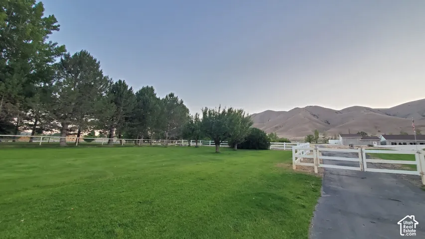 Expansive lawn area featuring mature trees, a white perimeter fence, and mountain scenery