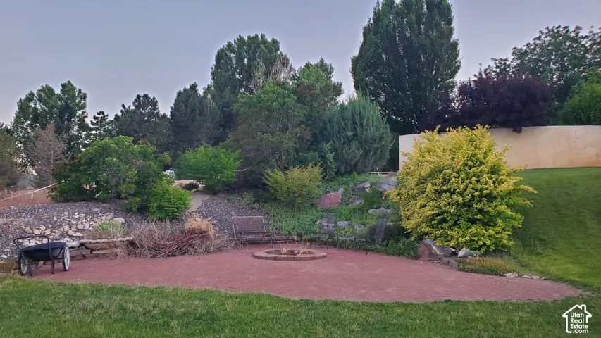 Spacious outdoor patio area featuring a built-in fire pit, surrounded by lush landscaping and mature trees
