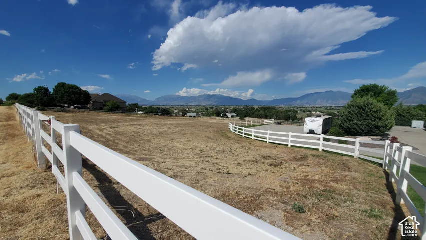 Expansive parcel featuring a white post-and-rail fence, a paved driveway, mature trees, and distant mountain ranges