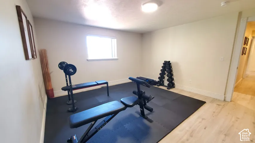 Dedicated fitness space featuring a rubber mat flooring, recessed ceiling lighting, a single window, and light wood-finish flooring extending into the hallway