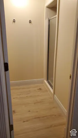 Shower enclosure with frosted glass door, light wood-finish flooring, and white baseboards