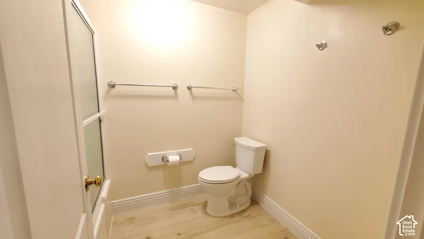 Bathroom featuring a white toilet, wood-finish flooring, and white baseboards