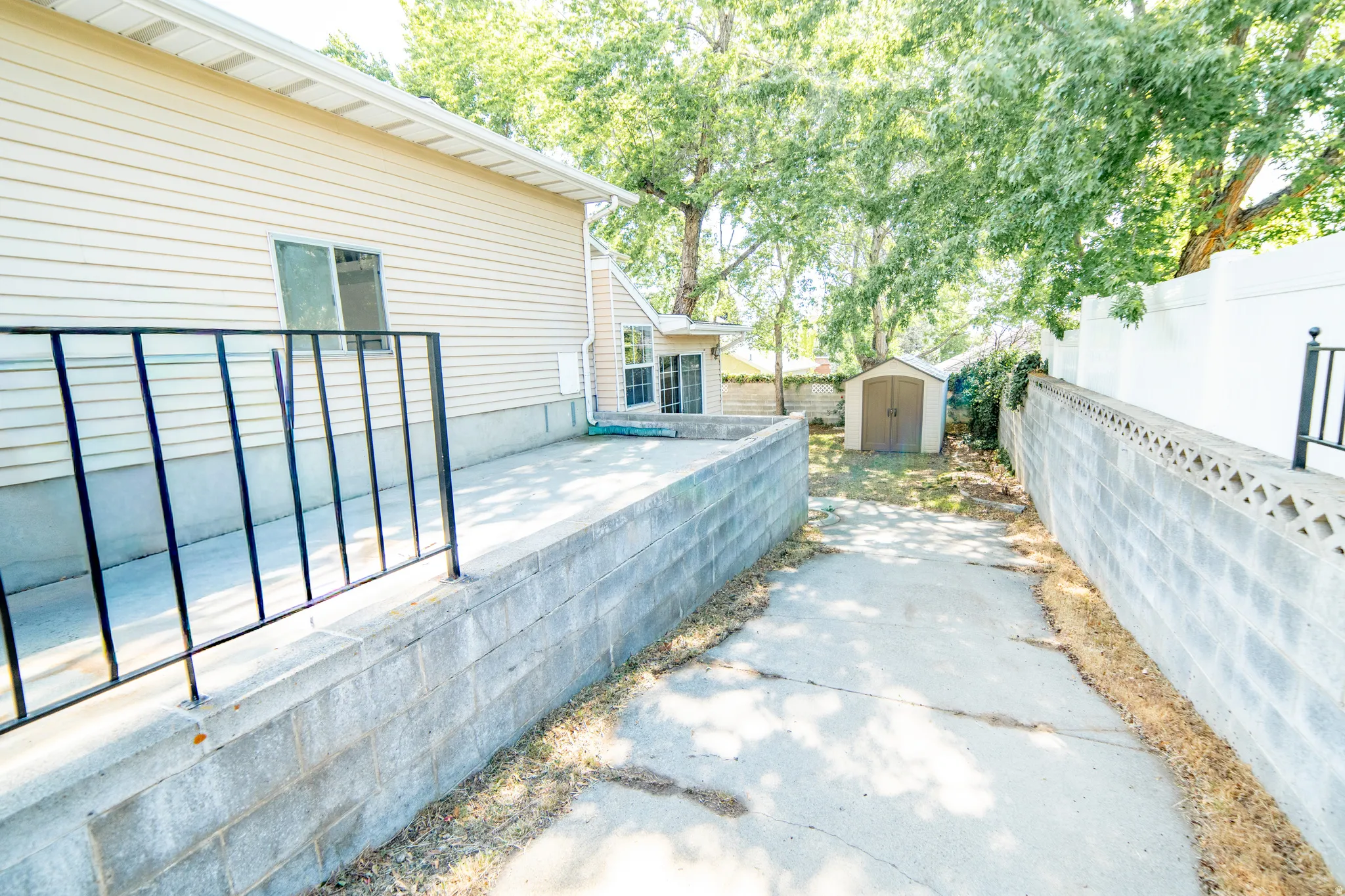 Rear exterior featuring vinyl siding, a concrete patio with black metal railing, and a storage shed